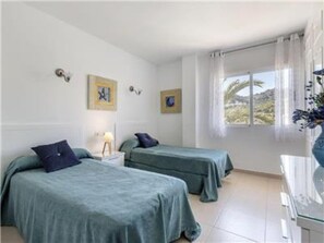 Ein Zimmer mit zwei Einzelbetten, einem Nachttisch, einem Fenster mit Vorhängen und Wandbildern.