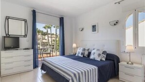 Un dormitorio con cama, televisor, escritorio y balcón con vistas.