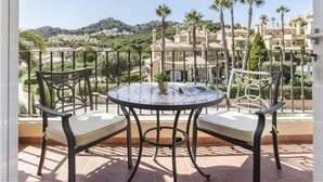 Una mesa redonda con dos sillas en un balcón que ofrece vistas a palmeras y edificios.