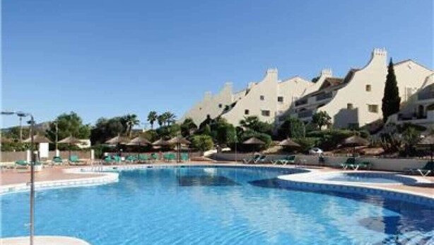 Una piscina con sillas de descanso y sombrillas, rodeada de edificios con arquitectura singular.