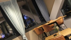 Un comedor moderno con una mesa y sillas de madera, ventanas grandes con cortinas y vistas a un paisaje urbano nocturno.