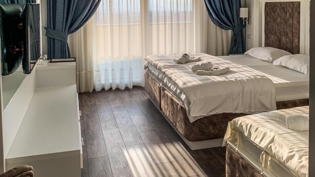 Habitación de hotel con dos camas, un escritorio con espejo y un ventanal con cortinas.