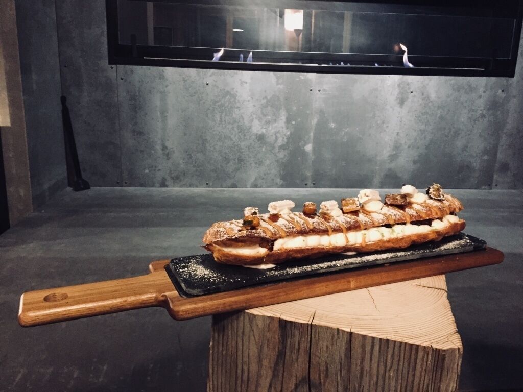 A dessert on a wooden board with a black tray, placed on a wooden stool in a room with a concrete wall and a window.