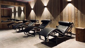 A room with wooden panel walls, black lounge chairs, and a mirror reflecting the chairs.