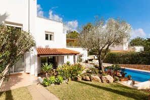 A modern house with a swimming pool, surrounded by a well-maintained garden and a clear blue sky.