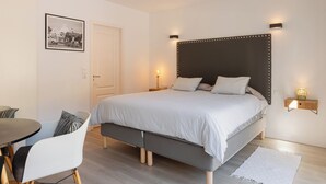 Een moderne slaapkamer met een bed, nachtkastjes, een stoel en een foto aan de muur.
