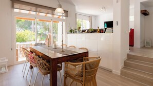 Een eethoek met een houten tafel, rieten stoelen, een hanglamp en uitzicht op groen.