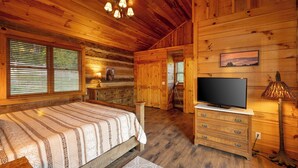 Quarto de cabana de toras com cama, penteadeira, televisão e lareira.
