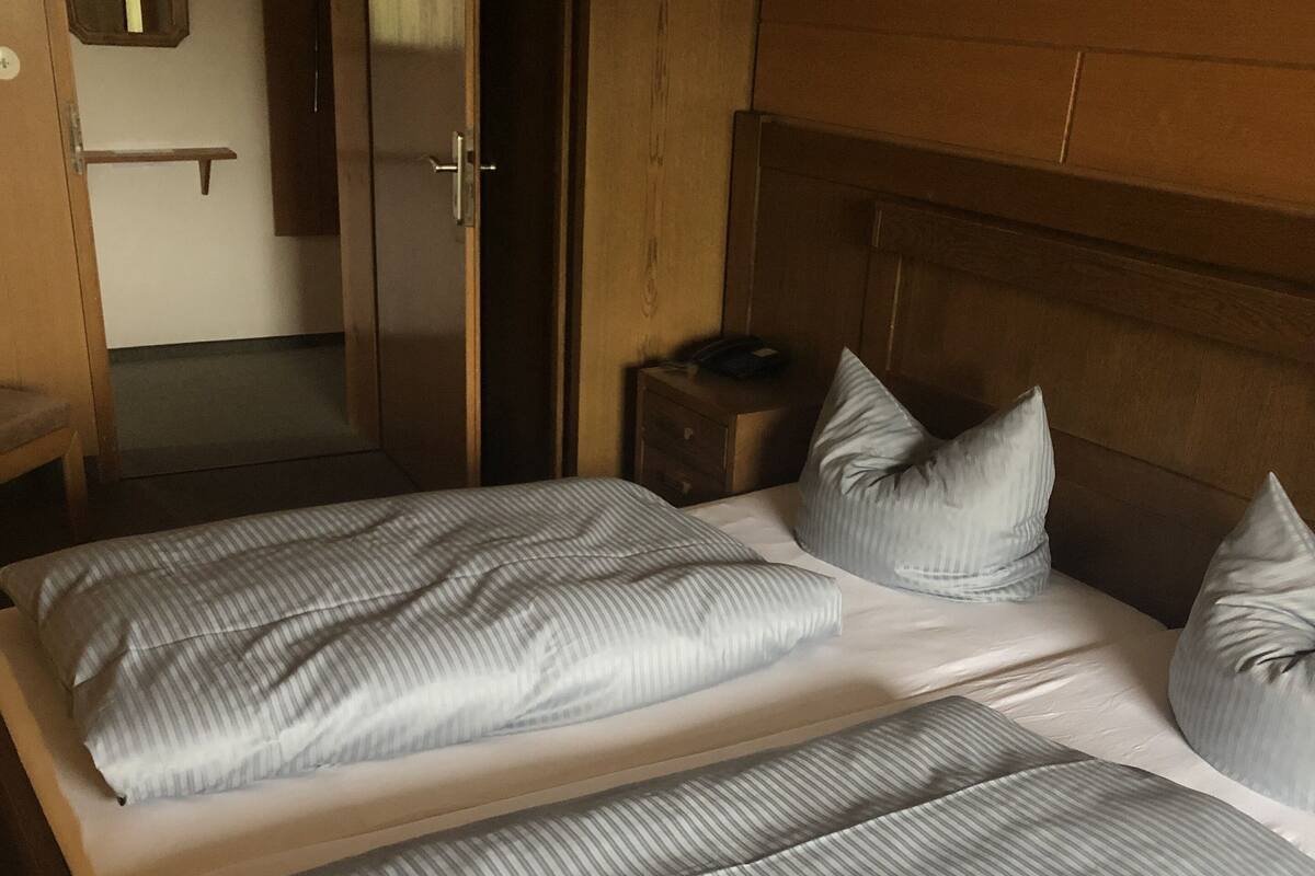 Een tweepersoonsbed met gestreepte beddengoed in een kamer met houten lambrisering en een nachtkastje.