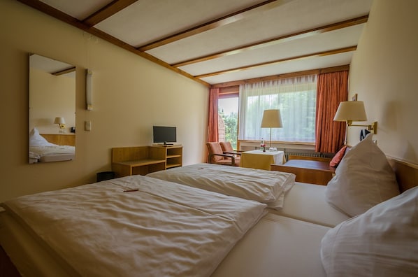A hotel room with two beds, a desk, a chair, a TV, and a window with curtains. - Wagners Hotel im Fichtelgebirge (Warmensteinach)