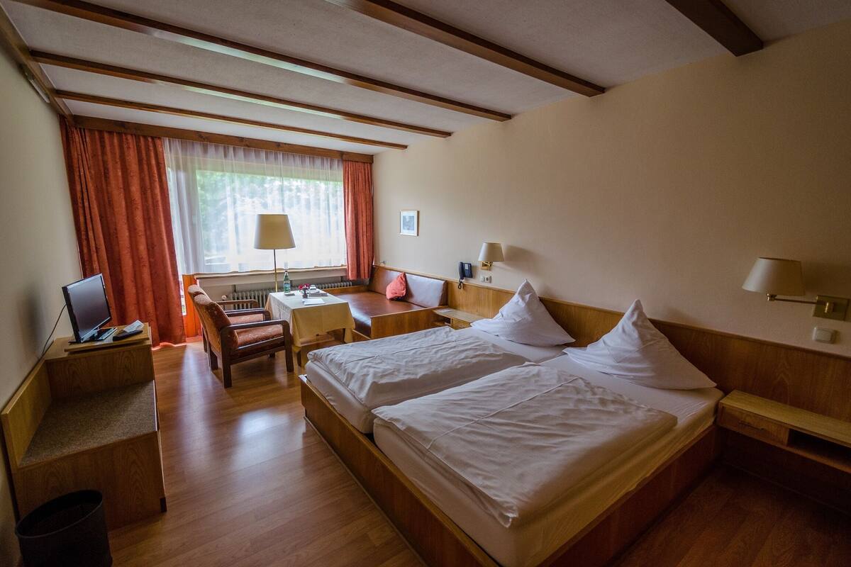 Een hotelkamer met een houten bed, een bureau, een stoel, een lamp en een raam met gordijnen.