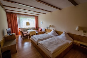 A hotel room with a wooden bed, a desk, a chair, a lamp, and a window with curtains. - Wagners Hotel im Fichtelgebirge (Warmensteinach)