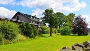 Een groot, twee verdiepingen tellend gebouw met een schuin dak, omgeven door een verzorgd gazon en diverse bomen.