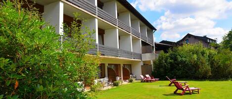 A hotel with a two-story structure, a covered outdoor seating area with red chairs, and a well-maintained lawn.