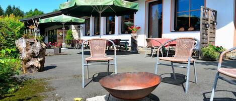 An outdoor seating area with wicker chairs and a metal table, green umbrellas, and a rustic wooden structure.