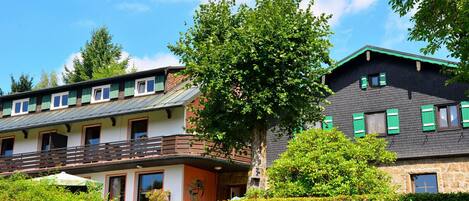 A multi-story building with balconies, a tree in front, and a hedge.