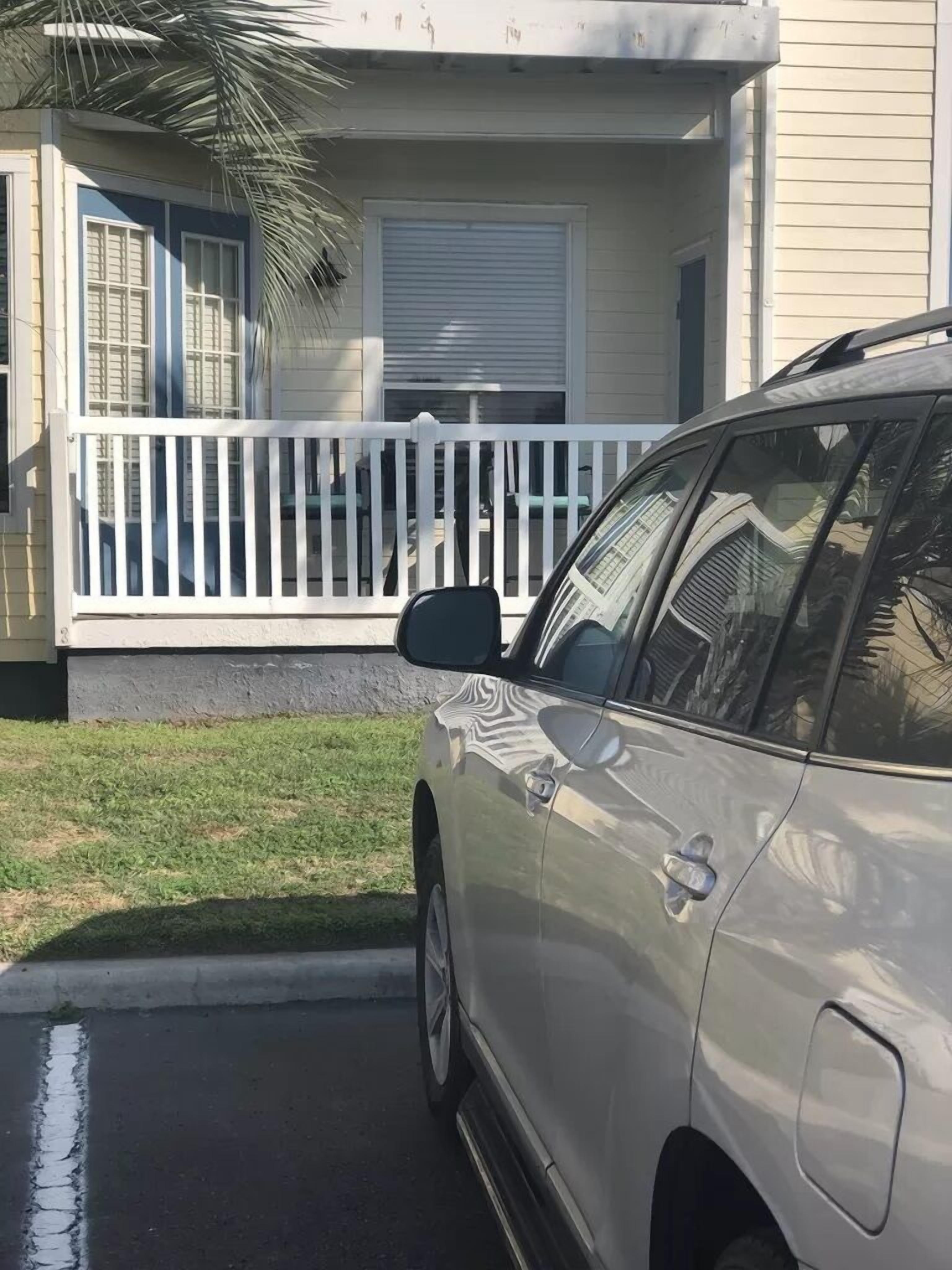Un coche blanco estacionado frente a una casa con porche blanco y puerta de garaje.