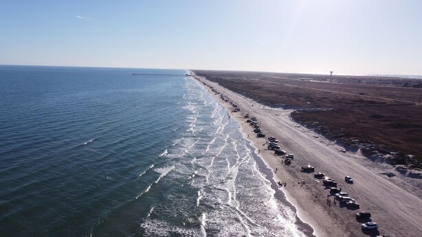 Vista aérea de una playa con una larga fila de coches aparcados a lo largo de la orilla.