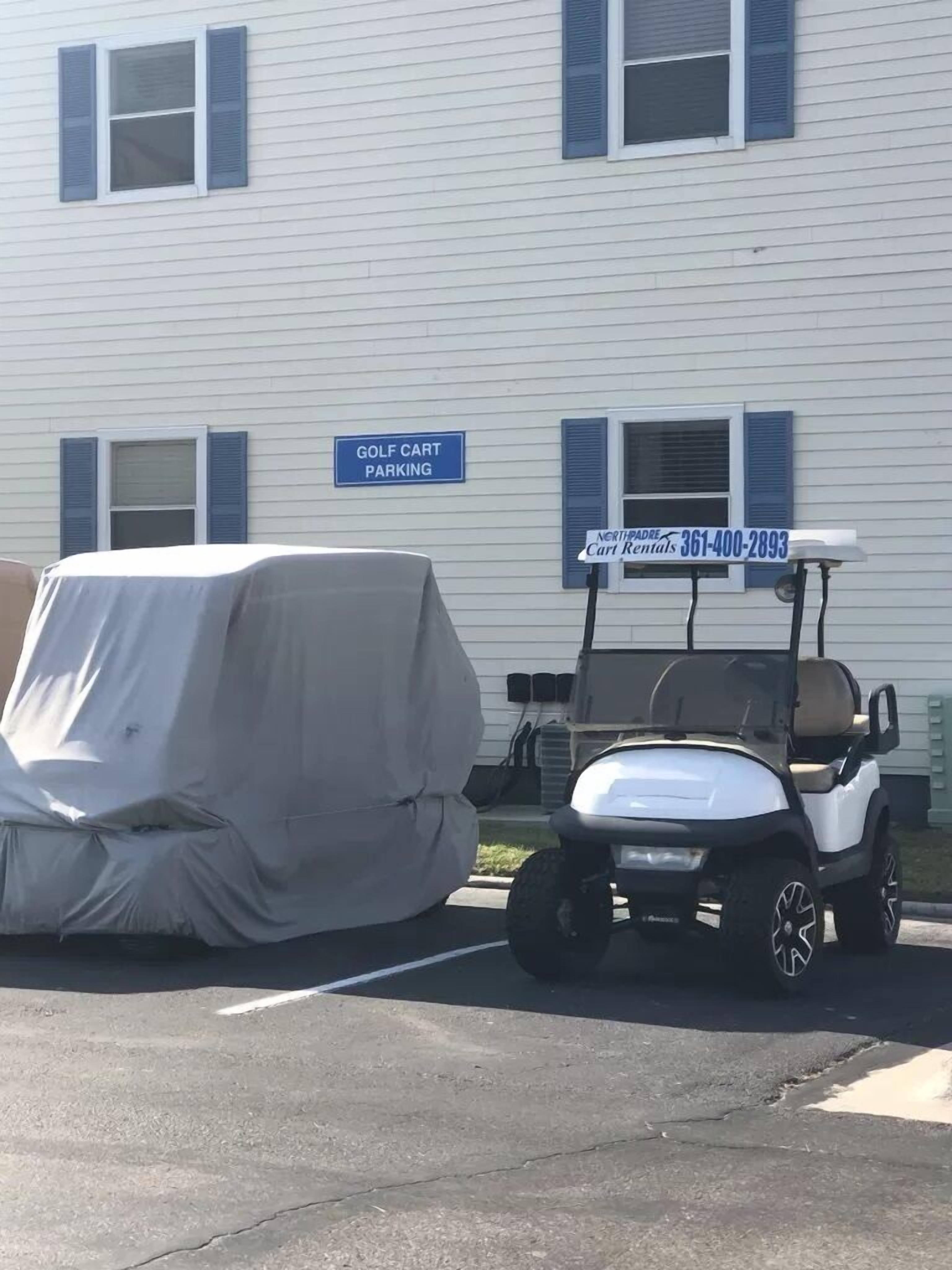 A covered vehicle and a golf cart parked in front of a building with a 'Golf Cart Parking' sign.