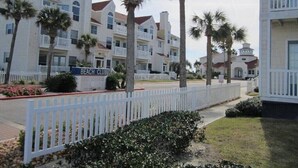 Zona residencial frente a la playa con edificios blancos, palmeras y una cerca blanca de piquete.