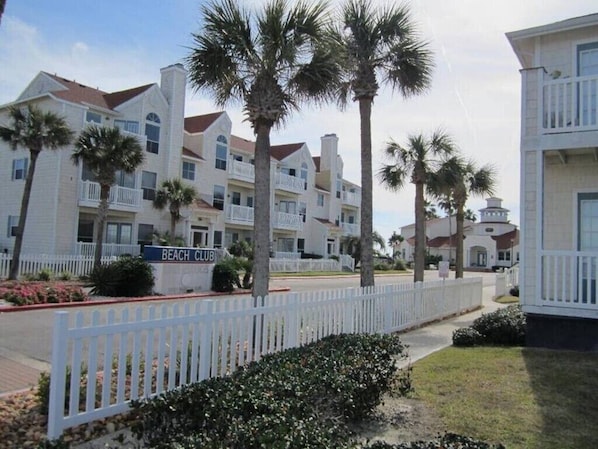 Zona residencial frente a la playa con edificios blancos, palmeras y una cerca blanca de piquete.