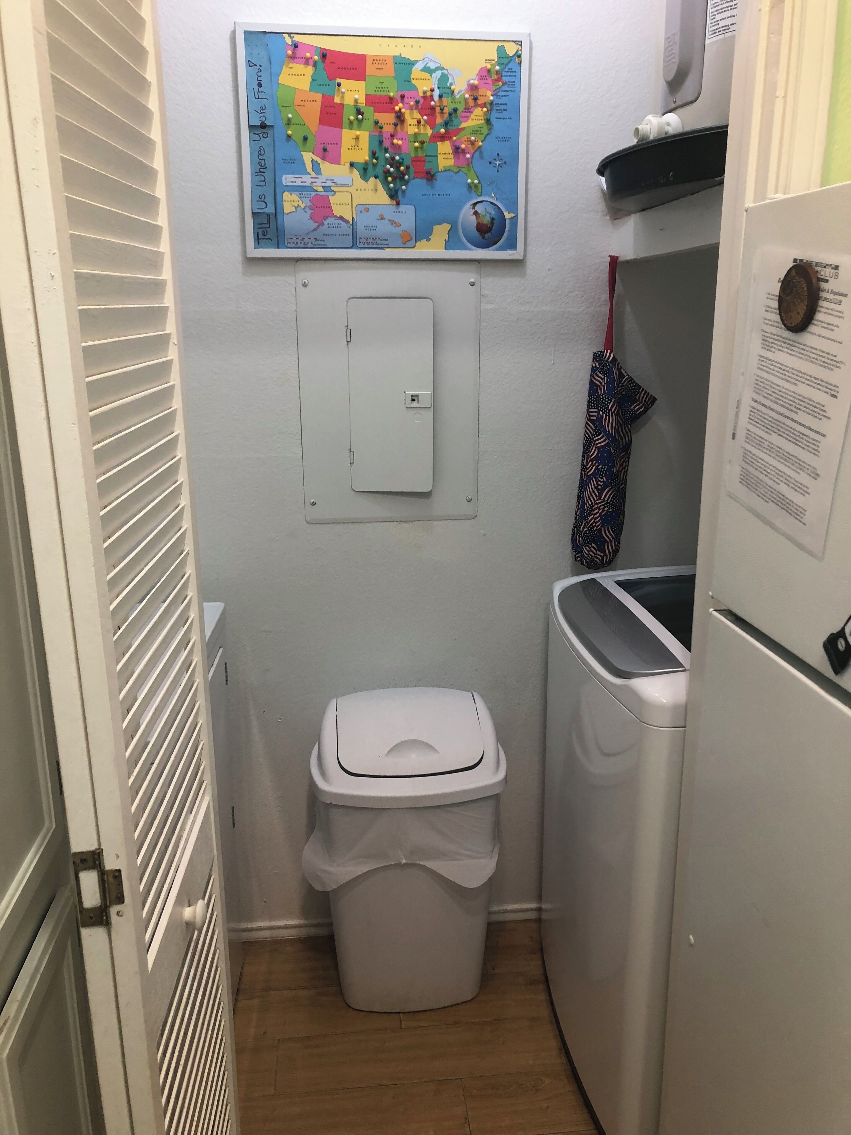 Une petite salle de bain comprenant des toilettes, une poubelle, un lave-linge et une carte des États-Unis accrochée au mur.