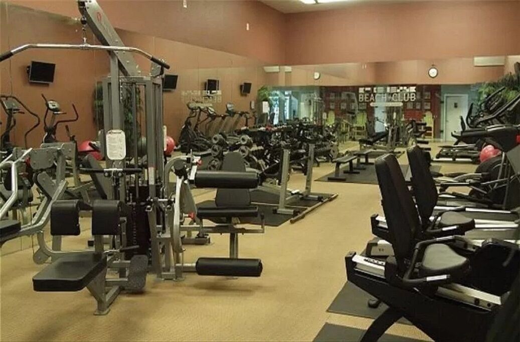 A gym with various exercise machines, including treadmills and weight stations, arranged in rows.