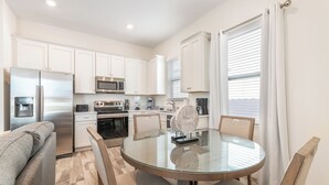 A modern kitchen with white cabinets, stainless steel appliances, and a glass dining table with chairs. - The Tiki Room 2BR Cottage | Margaritaville & Waterpark Access - 2954SR (Kissimmee)