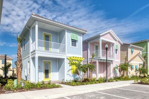 A row of colorful, two-story townhouses with balconies, a small garden area, and a clear sky.