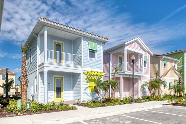 Una hilera de casas urbanas coloridas de dos pisos, con balcones, un pequeño jardín y cielo despejado.