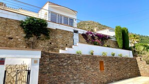 A modern house with a stone facade, a white upper level, and a small garden with purple flowers. - Property with modern equipment, sea views,air conditioning, fibre optic internet (Roses)