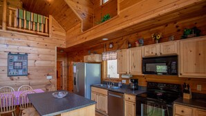 Interior de una cabaña de madera con cocina equipada: incluye refrigerador, microondas, estufa y armarios de madera.