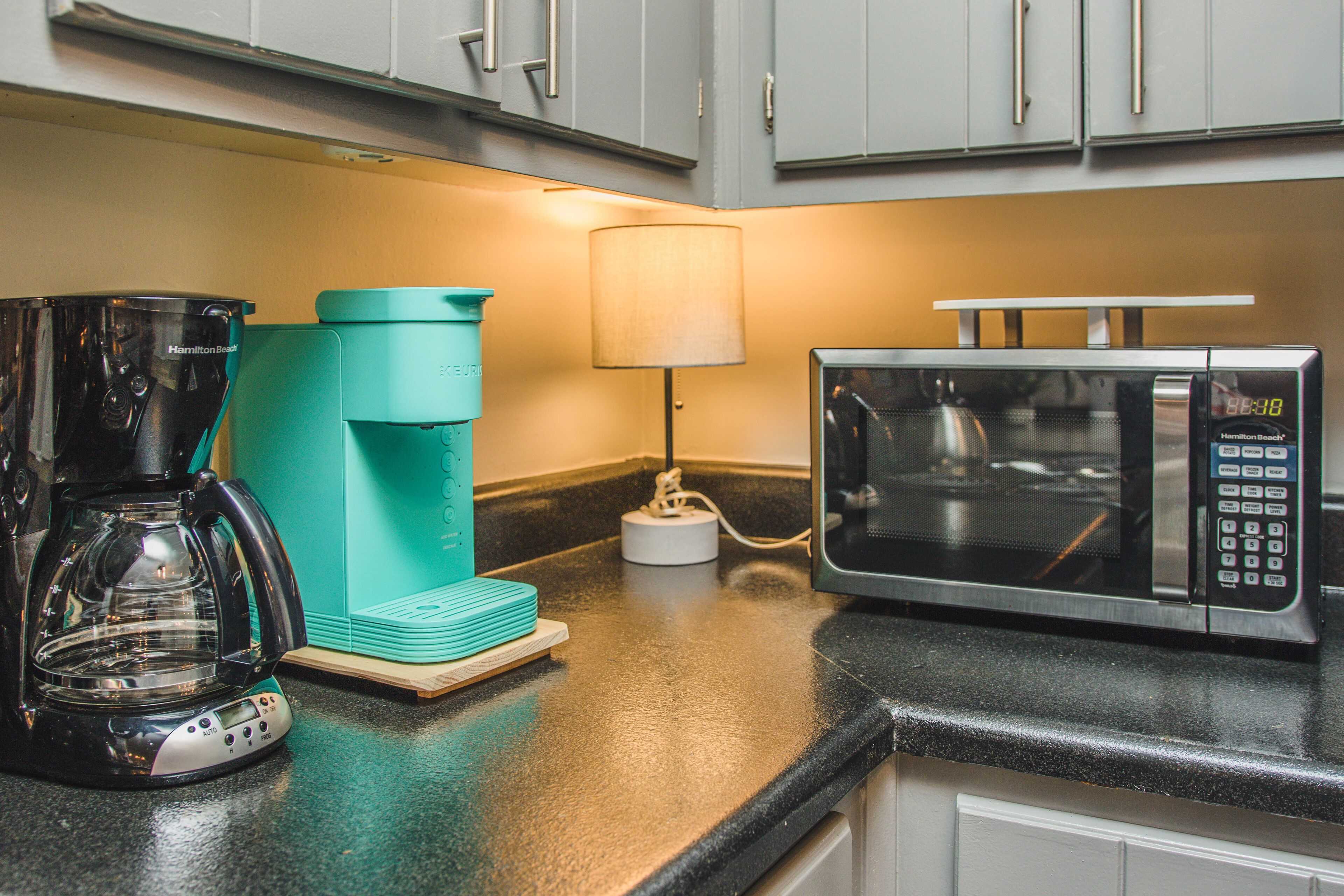 Una cocina con cafetera, microondas y una lámpara en la encimera.