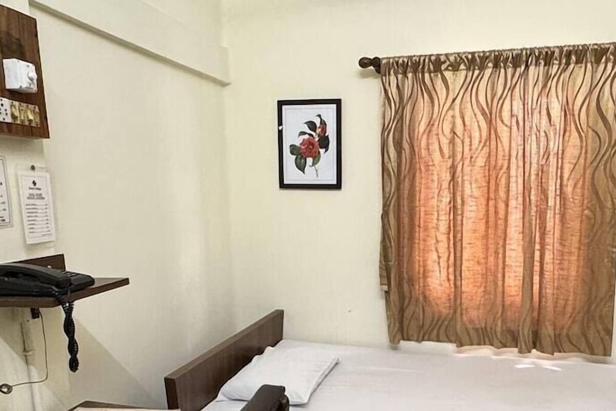 A bedroom with a bed, a nightstand, a wall-mounted telephone, and two framed floral pictures.