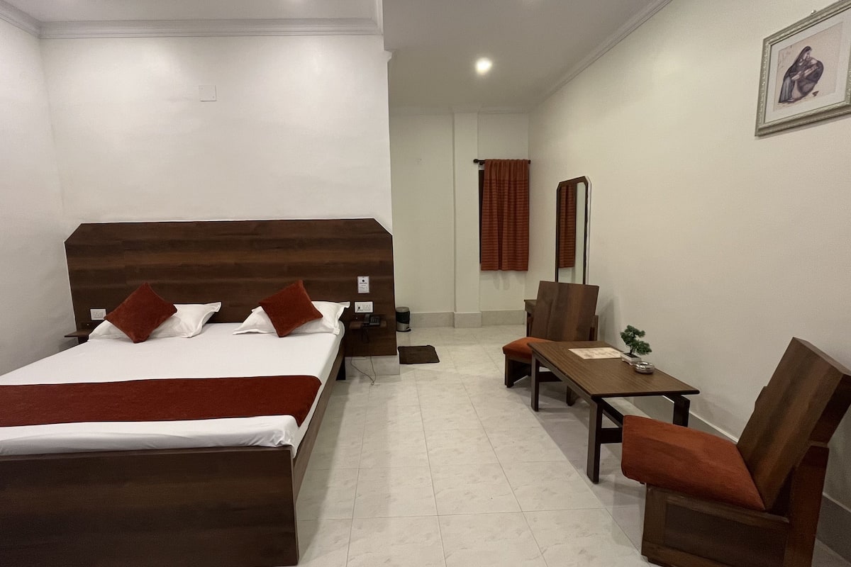 A hotel room with a large bed, a desk, a chair, and a small table.
