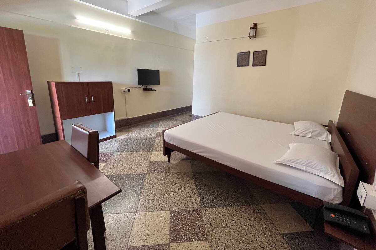 A hotel room with a bed, a desk, a wardrobe, a television, and a ceiling fan.