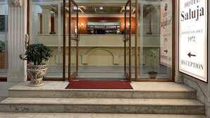 A hotel entrance with a reception desk, a potted plant, and a sign indicating the hotel name and year established. - Hotel Saluja (Siliguri)