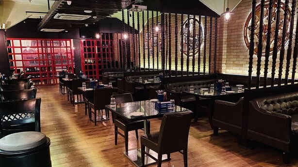 A restaurant with wooden flooring, leather seating, and a brick wall with decorative elements. - Hotel Saluja (Siliguri)