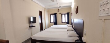 A hotel room with two beds, a TV mounted on the wall, a ceiling fan, and a window with curtains.