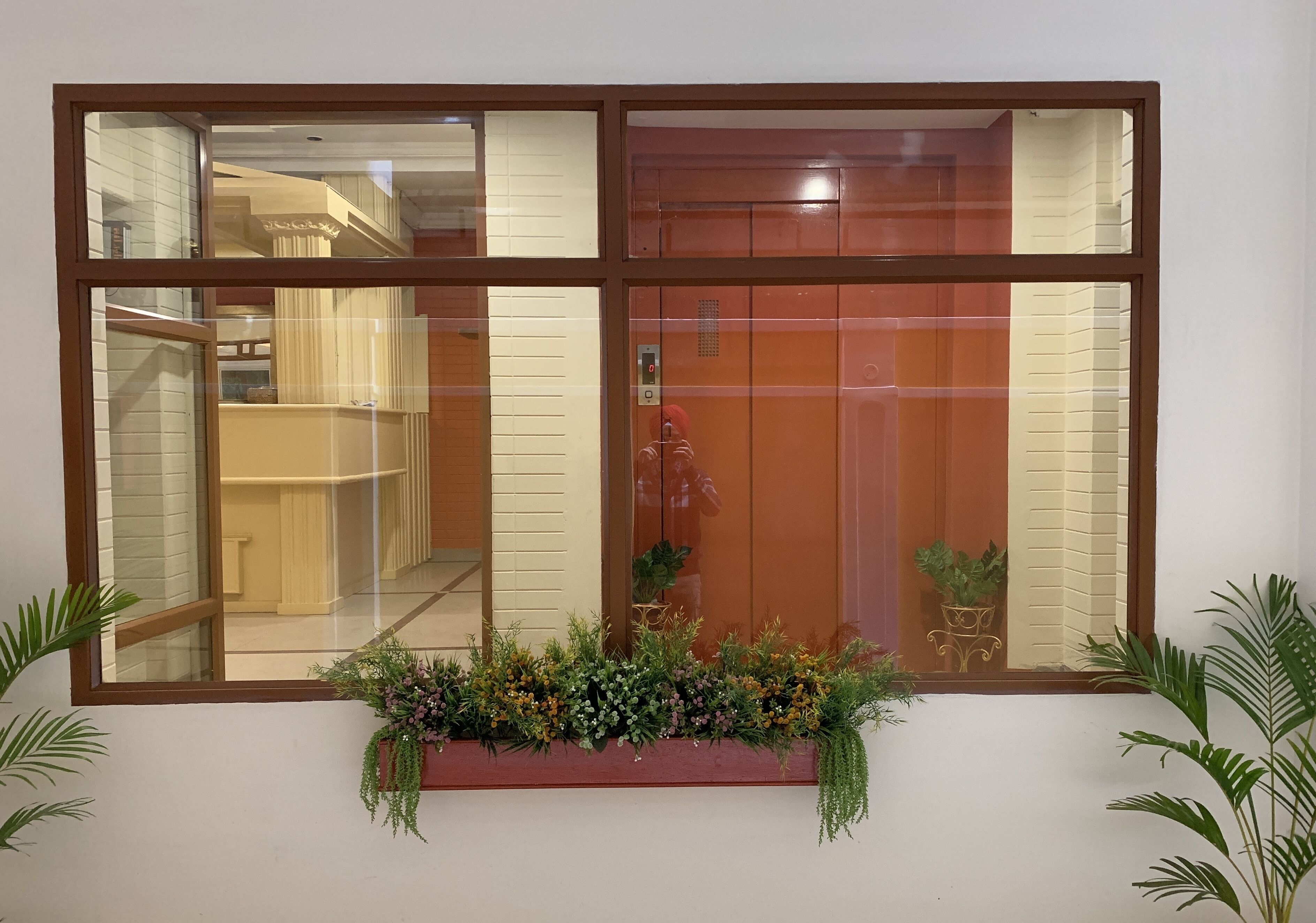 Une fenêtre donnant sur un intérieur en bois, une porte rouge et un jardinier avec des plantes vertes.