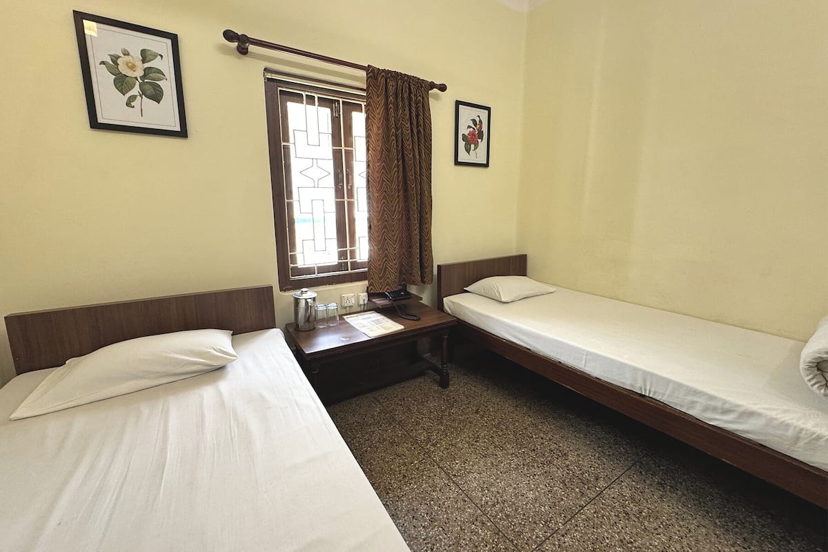 A room with two single beds, a window with curtains, and two framed floral pictures on the walls.