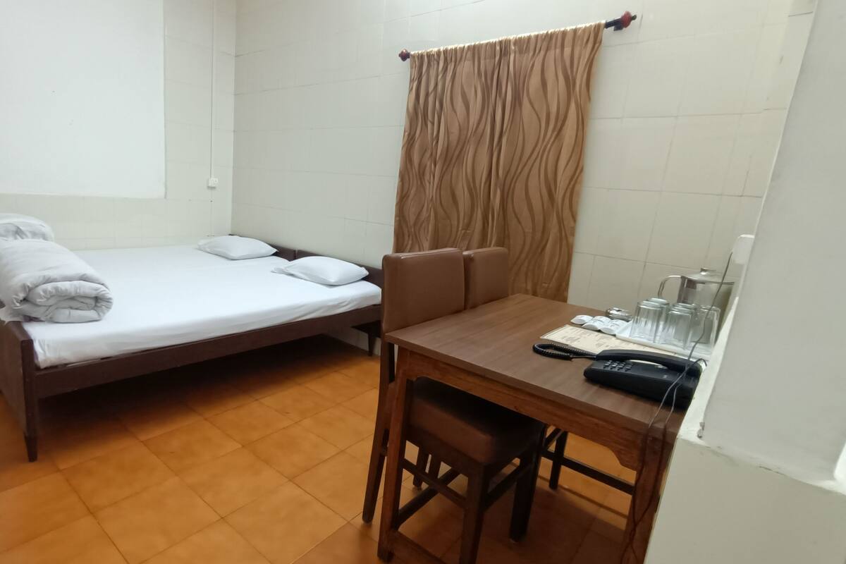 A small, clean room with a single bed, a wooden table with a chair, a telephone, and a curtain.