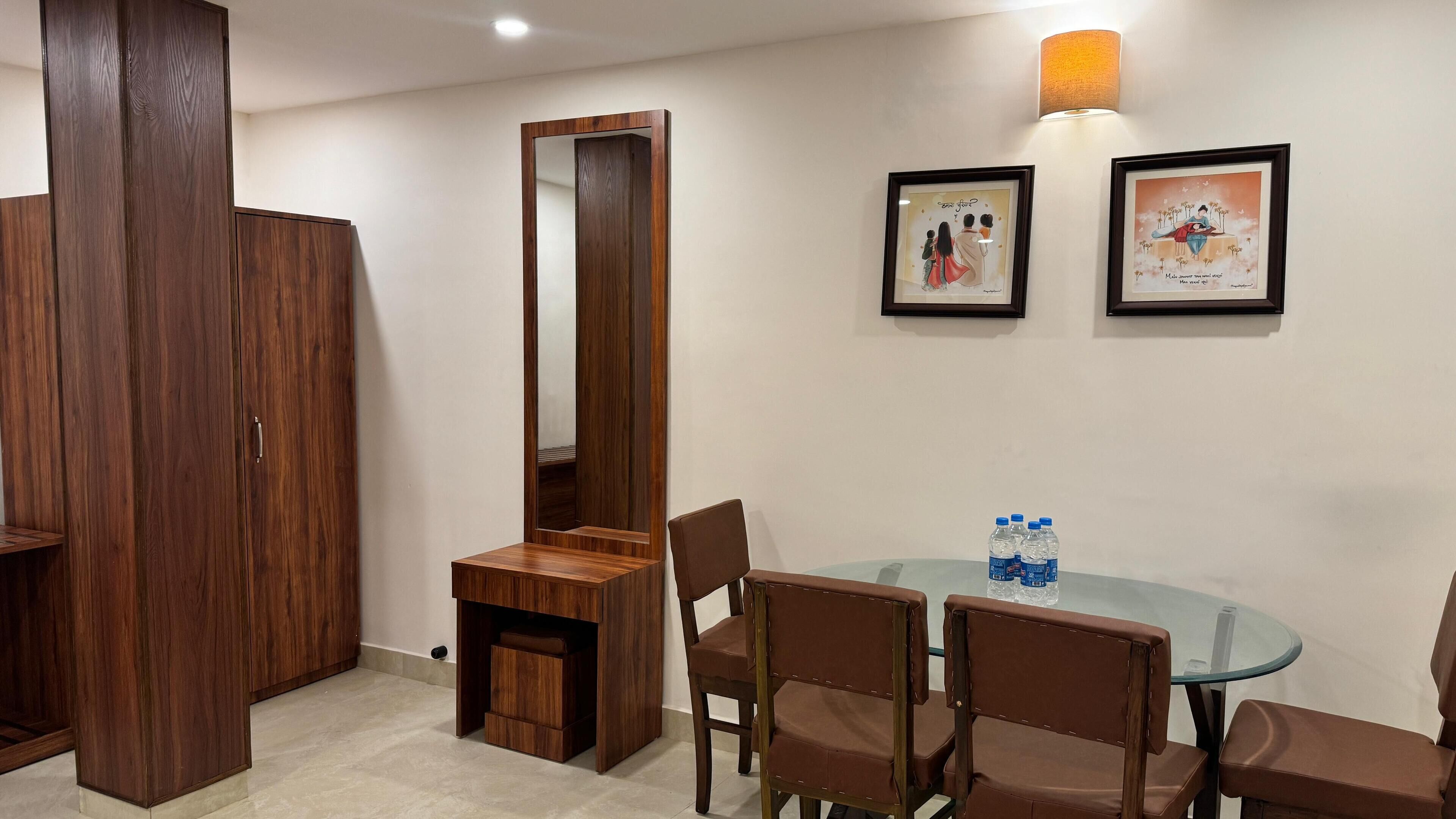 A room with a wooden wardrobe, a mirror, a round glass table with chairs, and two framed pictures on the wall.