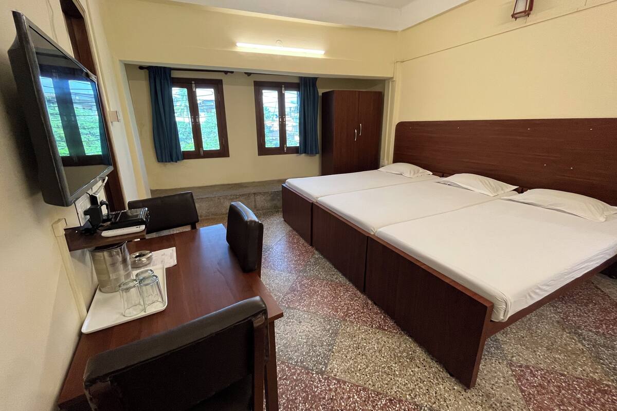 A hotel room with a bed, a desk with a computer, a television, and a window with curtains.