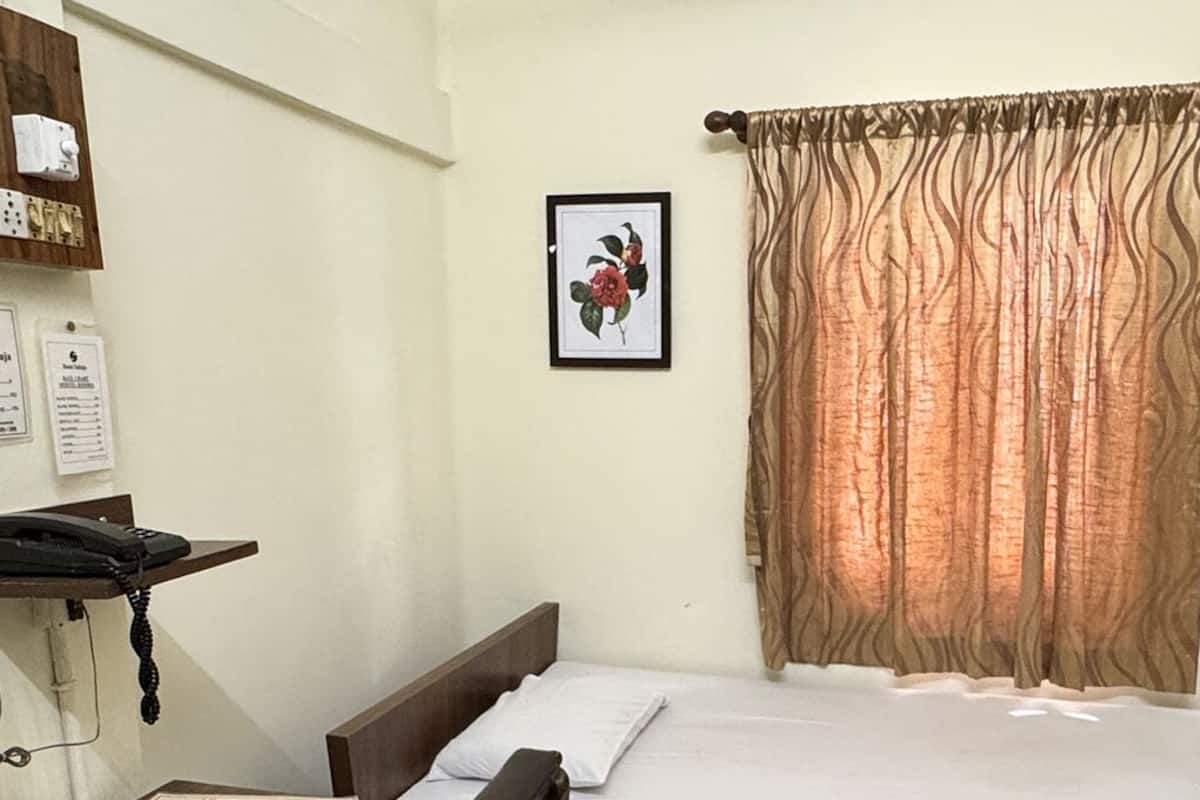 A hotel room with a bed, a telephone, a shelf with toiletries, and two framed floral pictures on the wall.