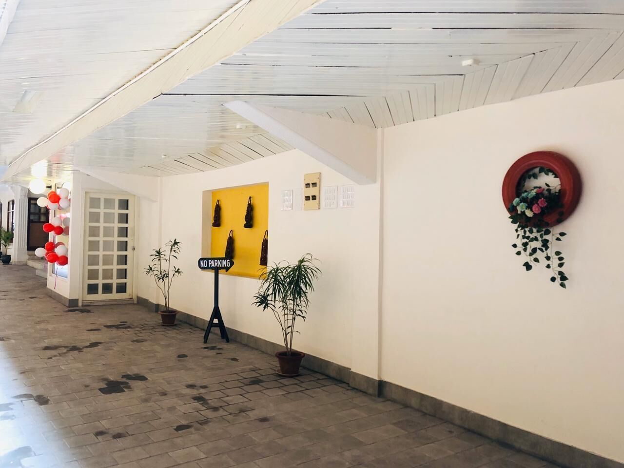 A corridor with a 'No Parking' sign, potted plants, and a yellow wall with artwork.