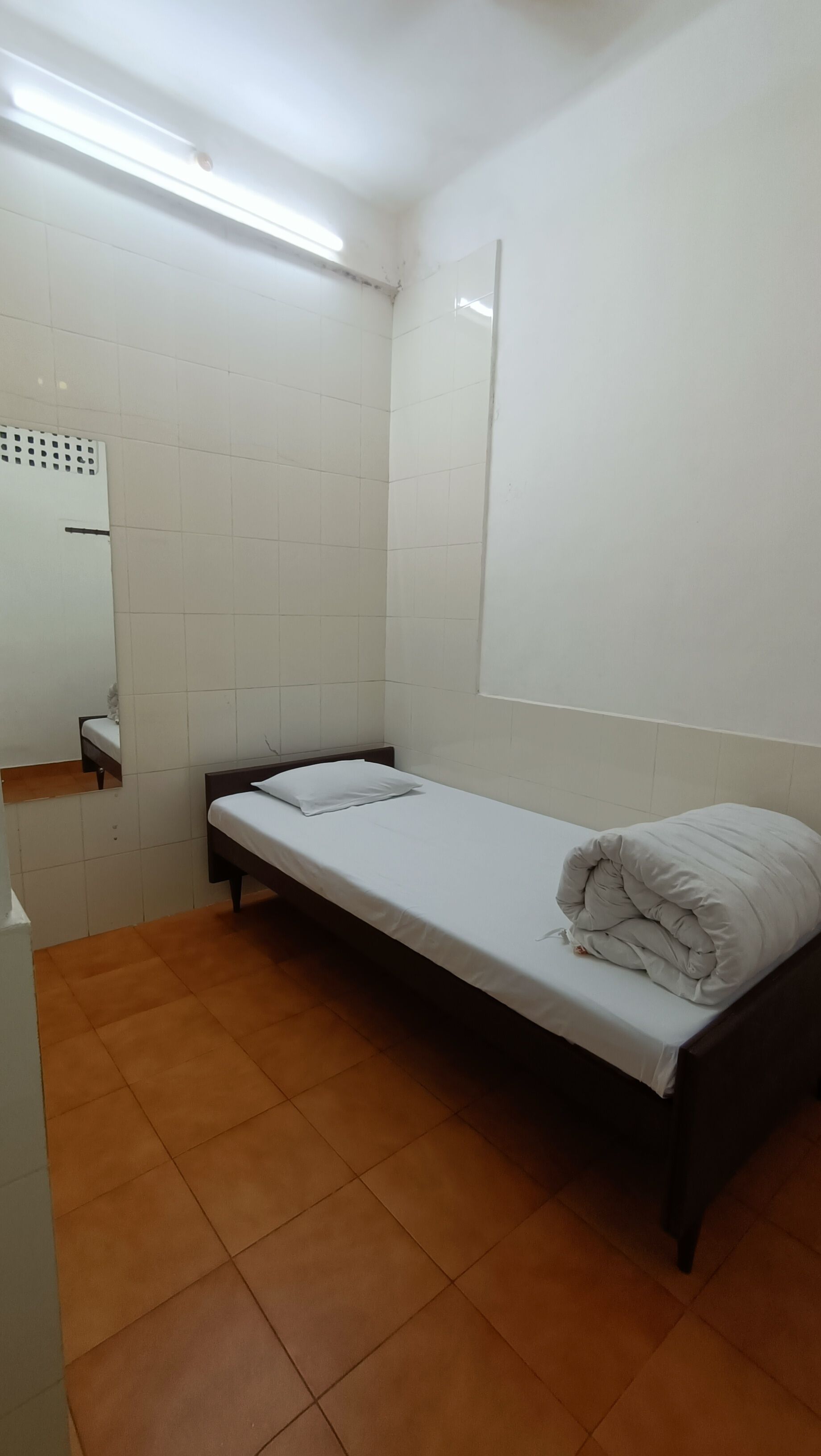 A small, single-bed room with white walls and a tiled floor.