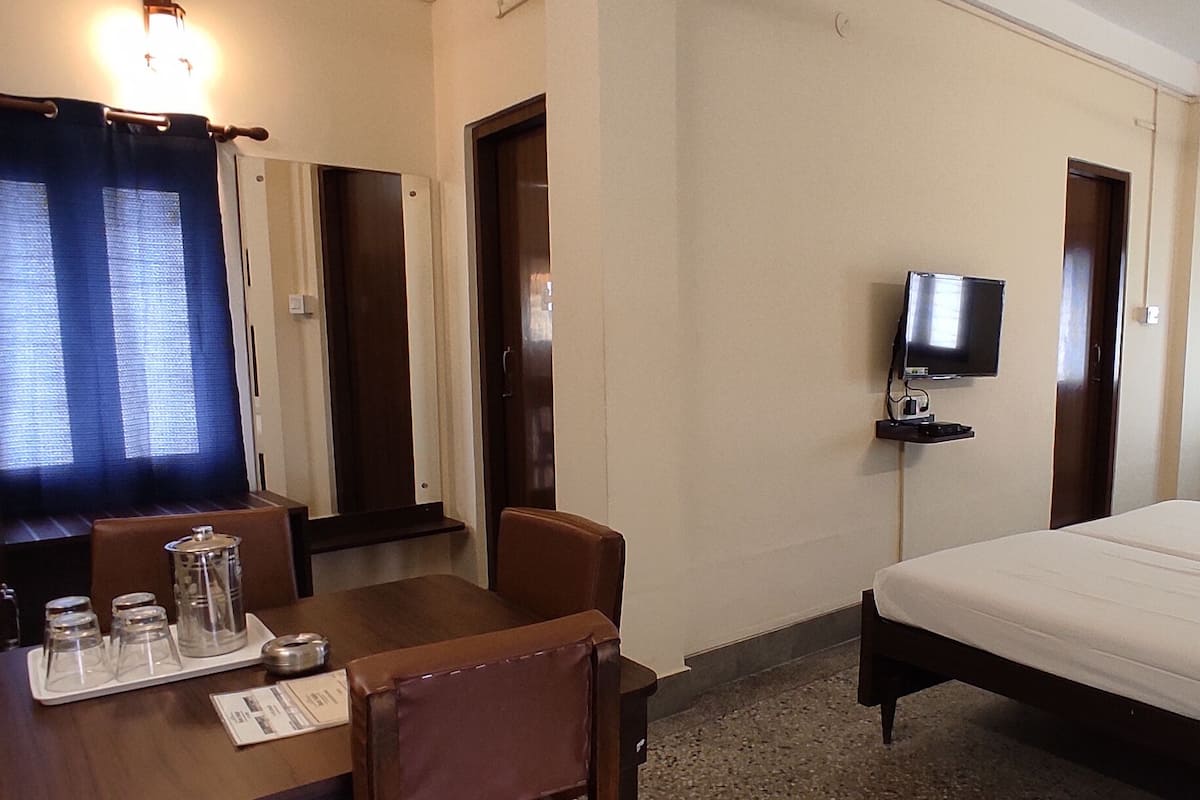 A hotel room with a bed, a desk with a chair, a television, and a window with curtains.