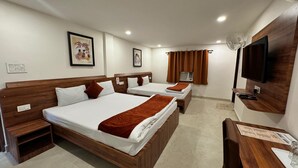 A hotel room with two beds, a TV, a fan, and artwork on the walls. - Hotel Saluja (Siliguri)