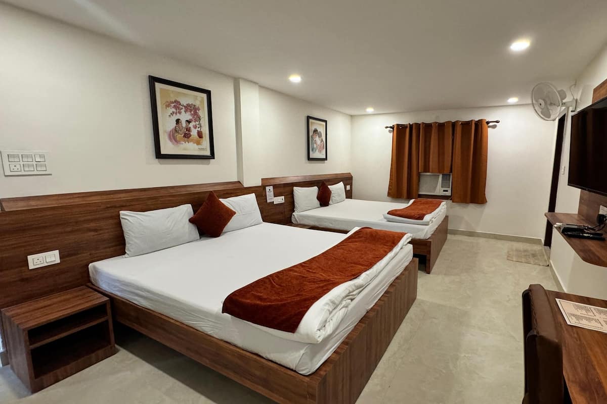 A hotel room with two beds, a TV, a fan, and artwork on the walls.